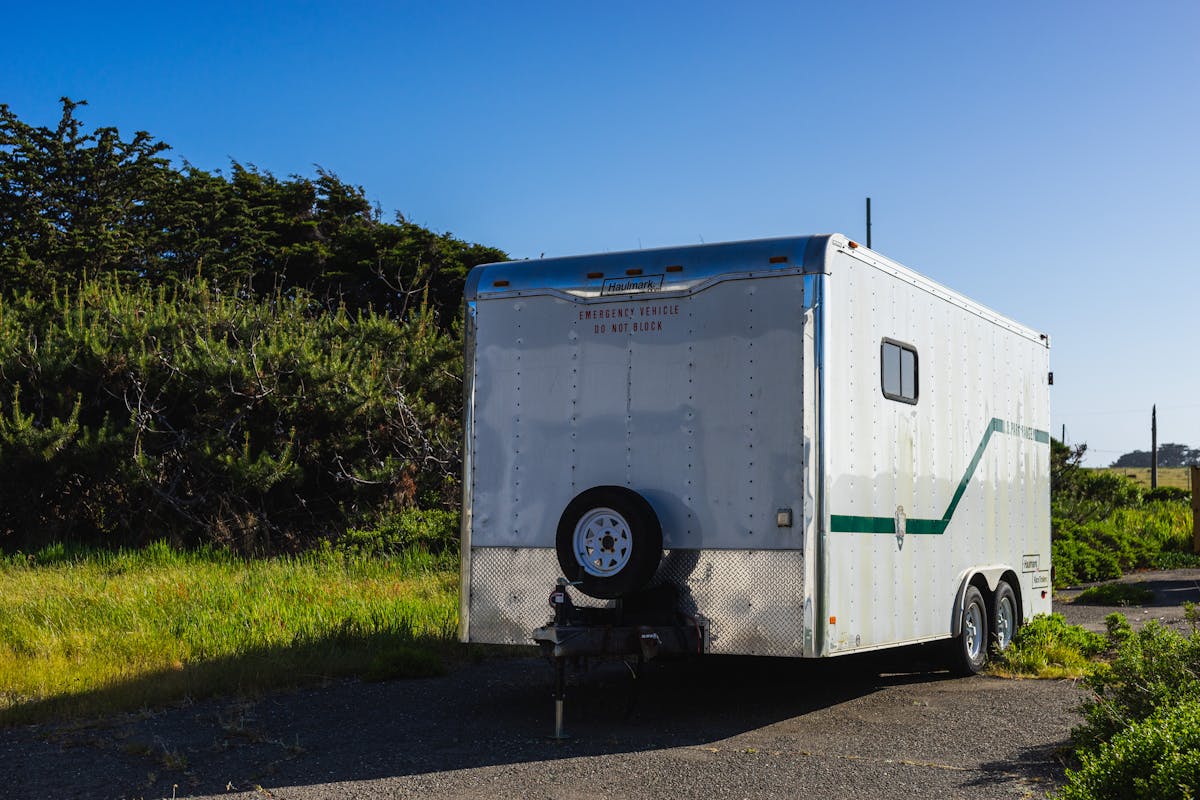 White RV trailer parked on a rural road surrounded by greenery under a clear sky