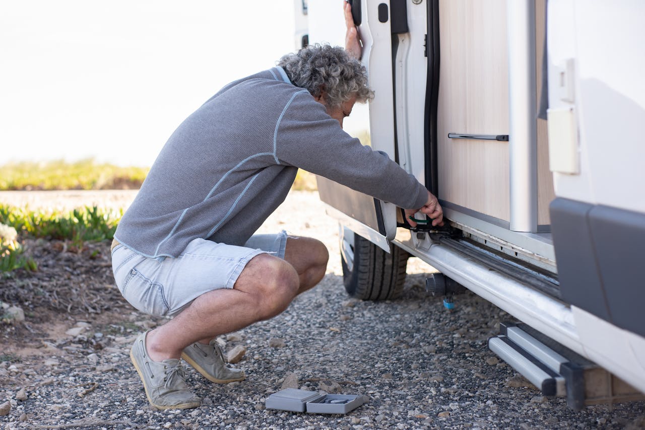 Man performing hands-on maintenance work on a camper van outdoors