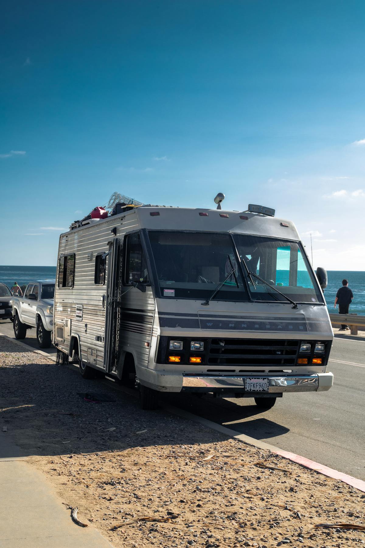 White RV travel trailer on a coastal asphalt road under clear blue sky
