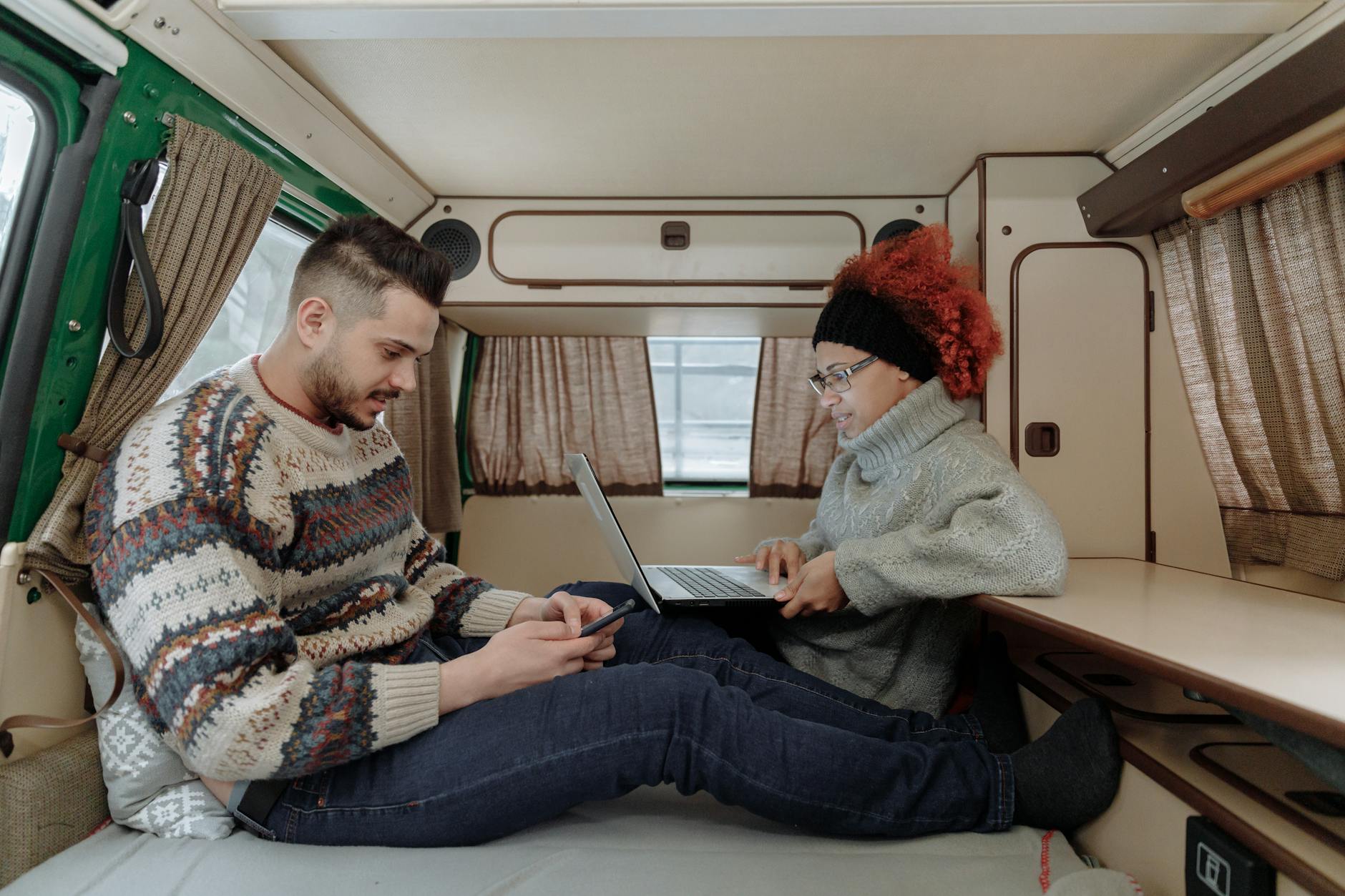 A couple working remotely on laptop and smartphone inside a campervan