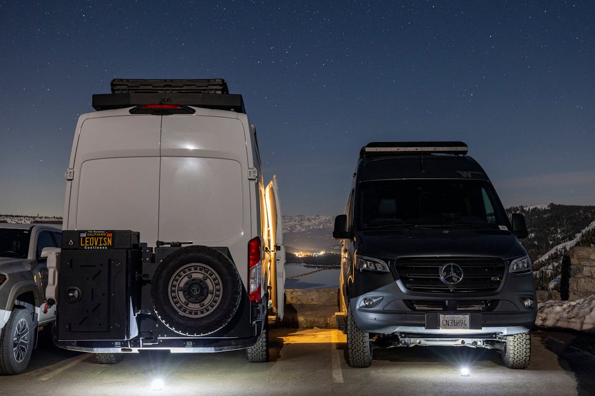 Two camper vans parked under a starry night sky in a winter mountain landscape, relying on battery power off-grid