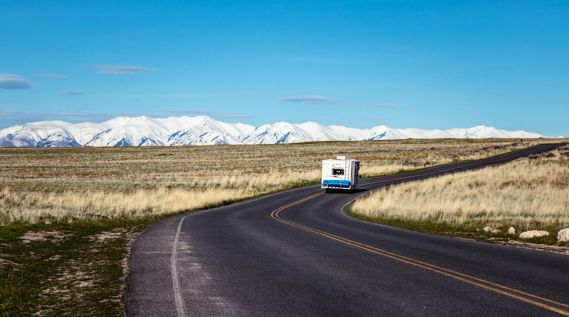 RV traveling down a winding mountain road with snow-capped peaks in the background