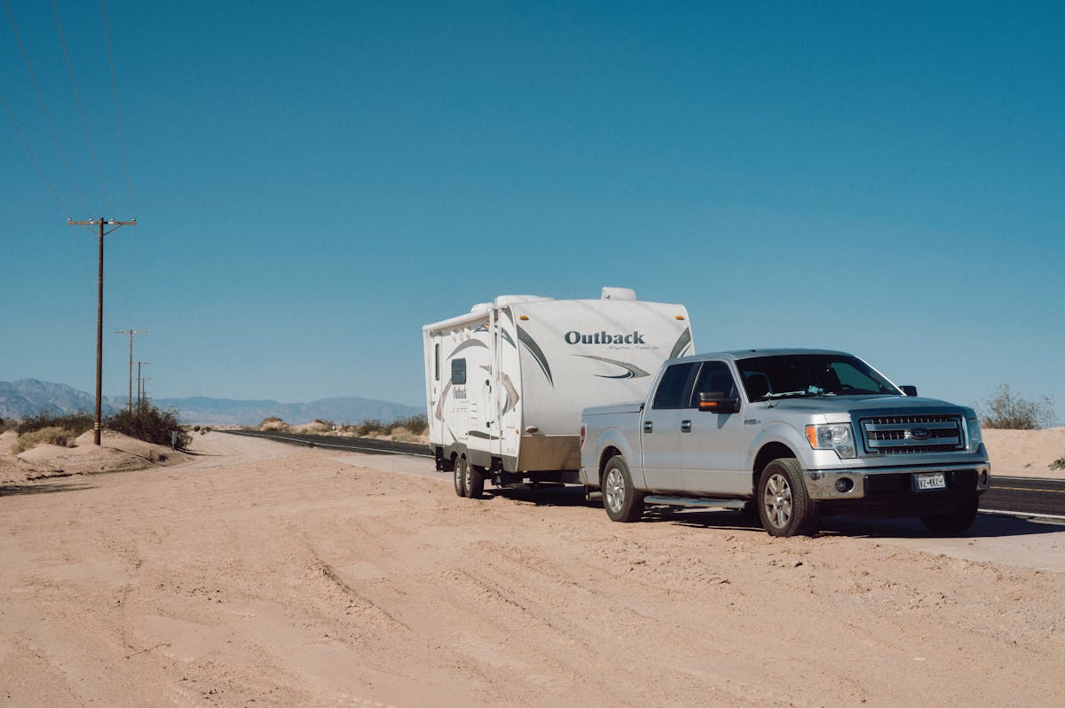 Silver truck towing a travel trailer on a desert road under clear blue skies