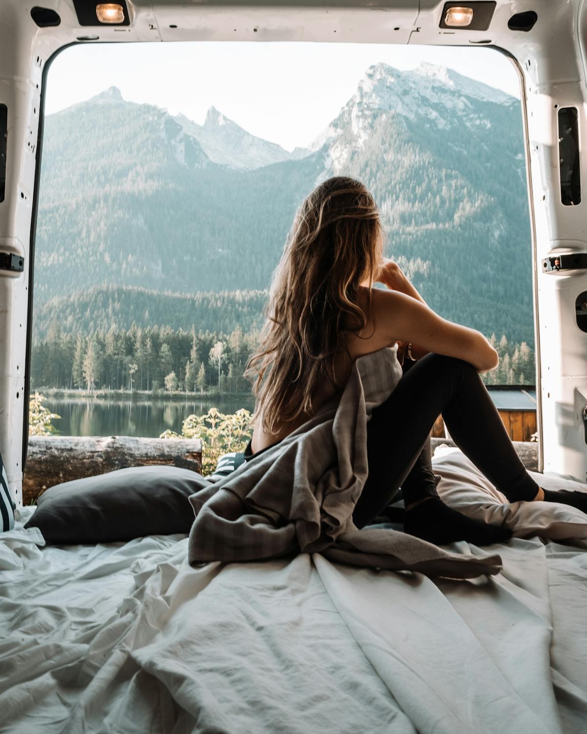 Woman sitting in the back of a camper van looking out at a mountain landscape